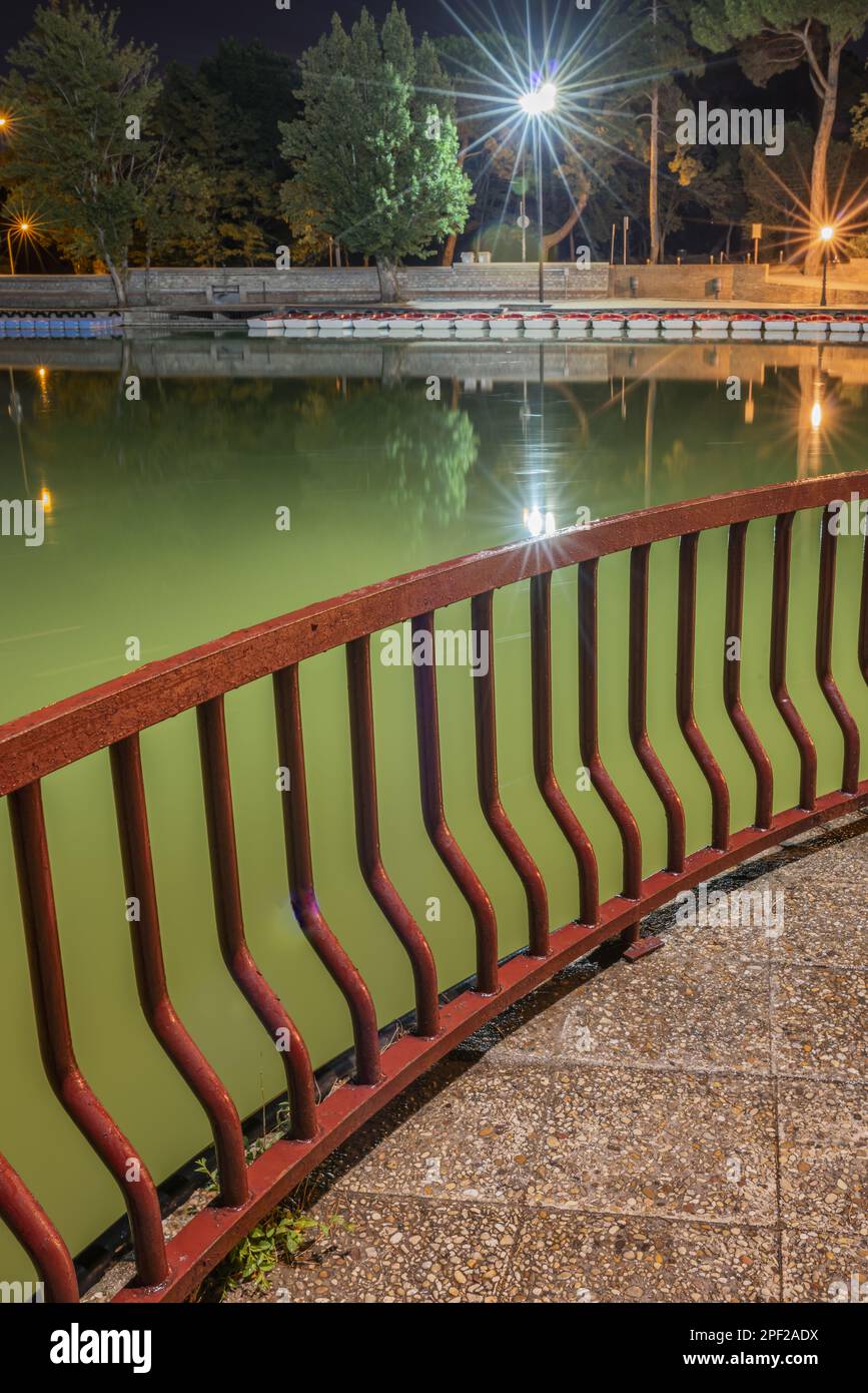 A night image of a red painted metal railing on the shore of a lake ...