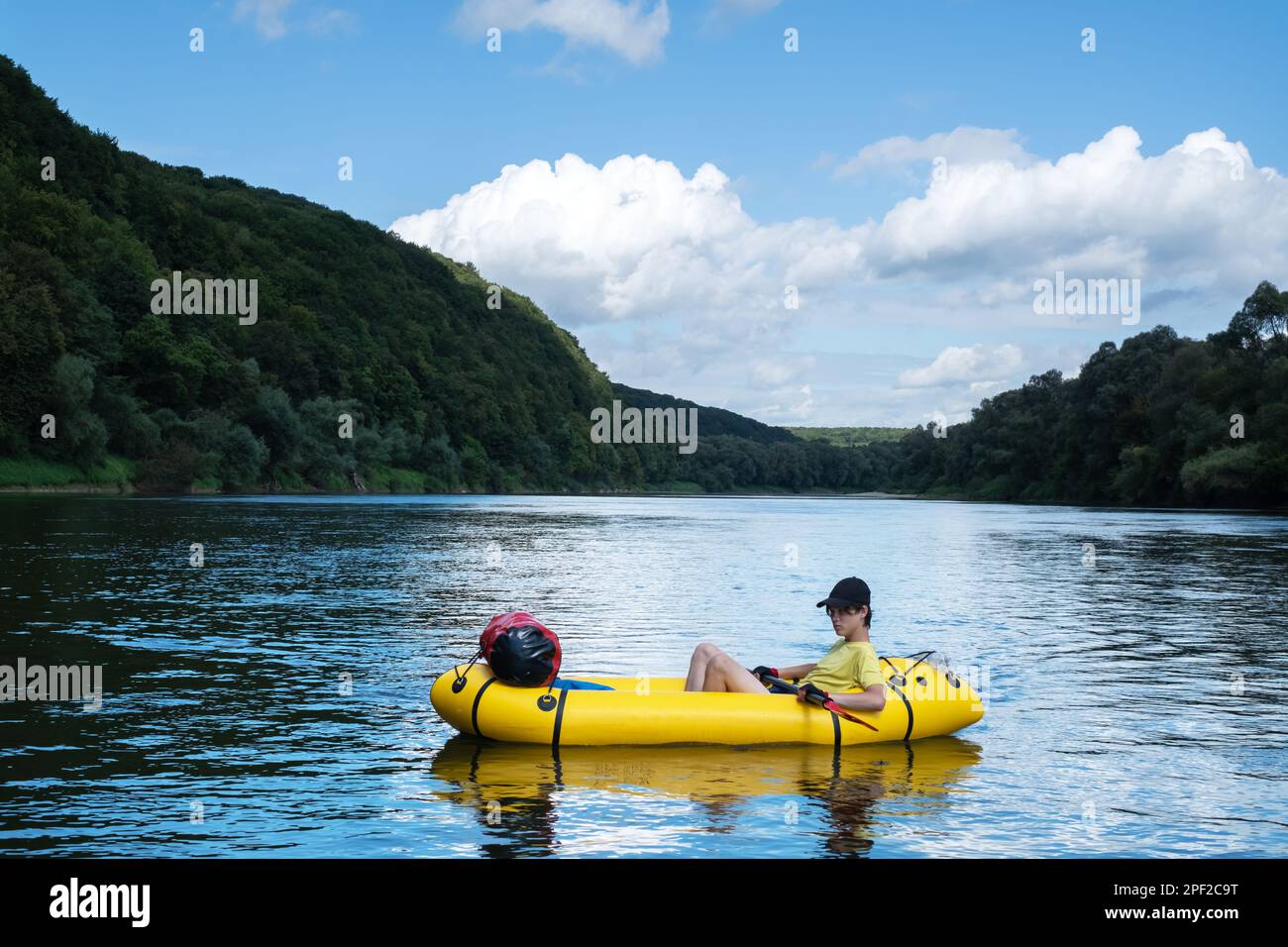 Young boy on yellow packraft boat with red padle on a sunrise river. Packrafting background. Active lifestile concept Stock Photo