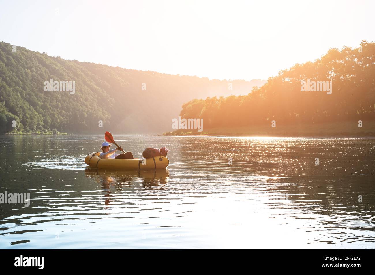 Tourist on yellow packraft boat with red padle on a beautiful river during sunset. Packrafting and active lifestile concept Stock Photo