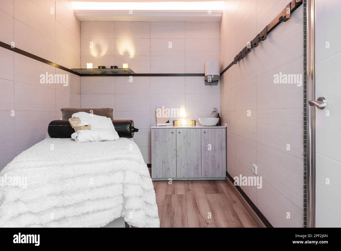 Cabin of a clinic for aesthetic treatments with a massage table, light bulbs similar to candles and a wooden sideboard Stock Photo