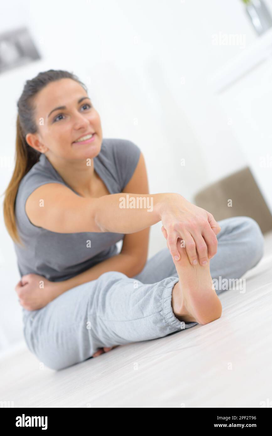 Young slim woman in the hood sitting on the yoga mat and pulling