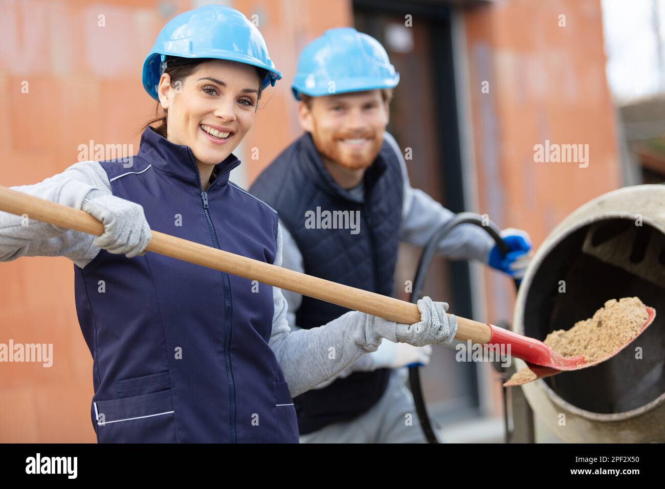 female builder loading sand into cement mixer Stock Photo