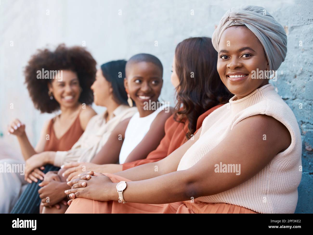 Young african american businesswoman sitting in a line with her coworkers against a wall outside in the city. Black female smiling while sitting Stock Photo