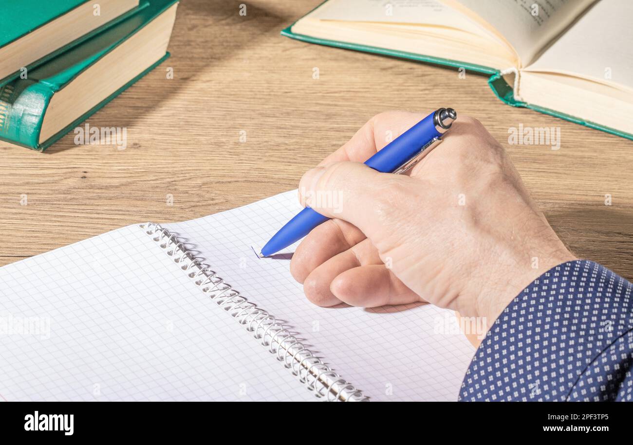 A man's hand with a blue pen makes notes in an open notebook on an ...