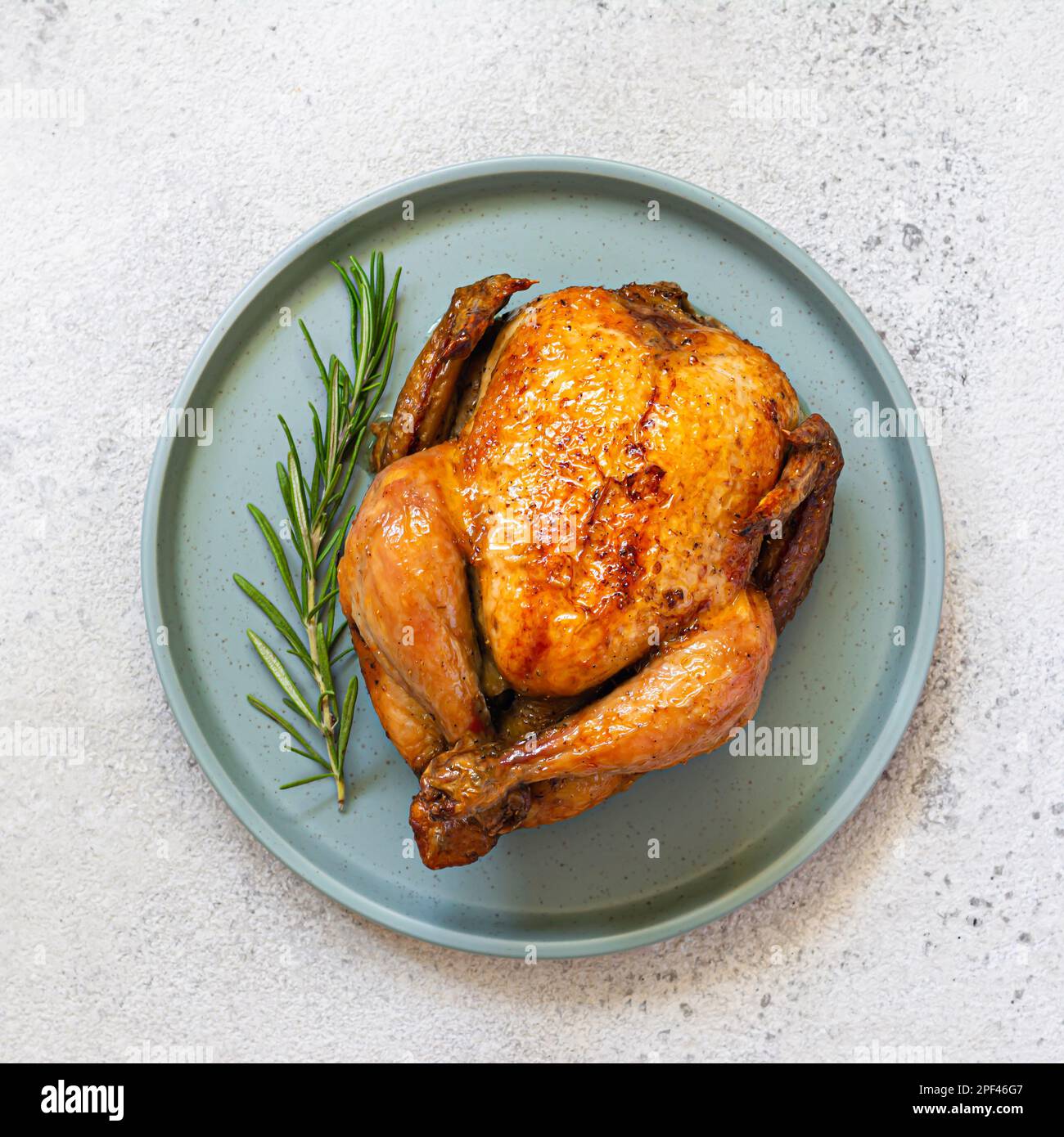 Whole baked (fried) chicken in spices with rosemary on a dish on  light background. Festive food for thanksgiving, birthday. Fast food, top view. Stock Photo