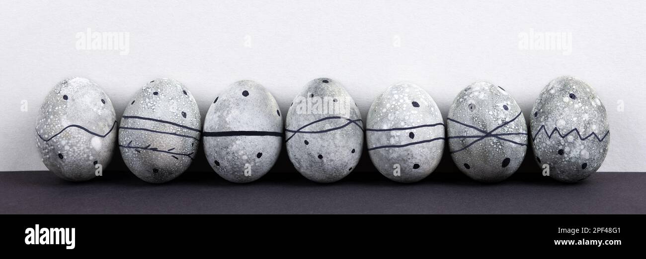 Seven grey Easter eggs in a black pattern on a grey background. Happy Easter concept. Banner Stock Photo