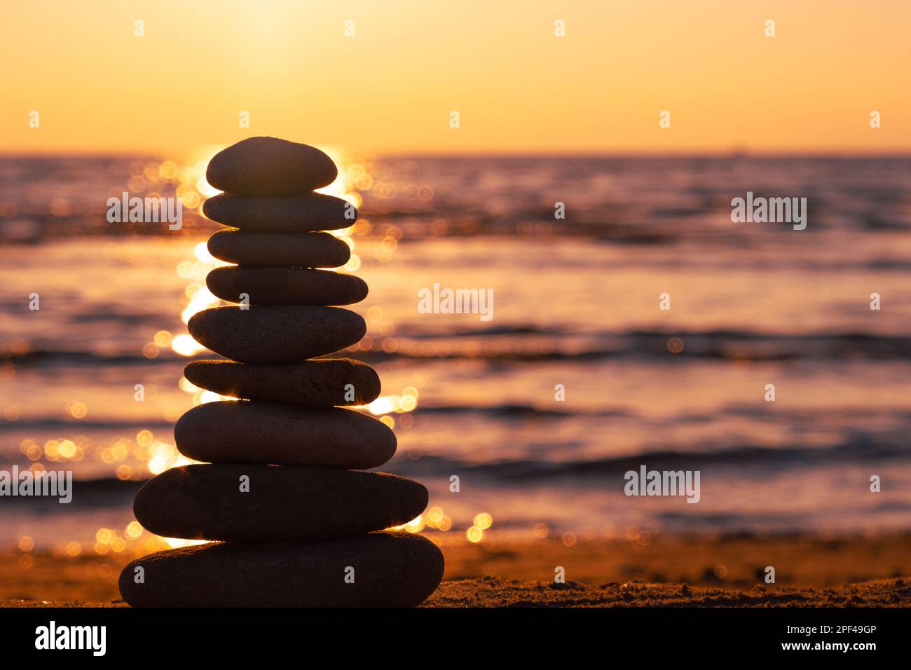 Balanced pebble pyramid silhouette on the beach on sunset with Sea on the background. Zen stones on the sea beach, meditation, spa, harmony, calmness. Stock Photo