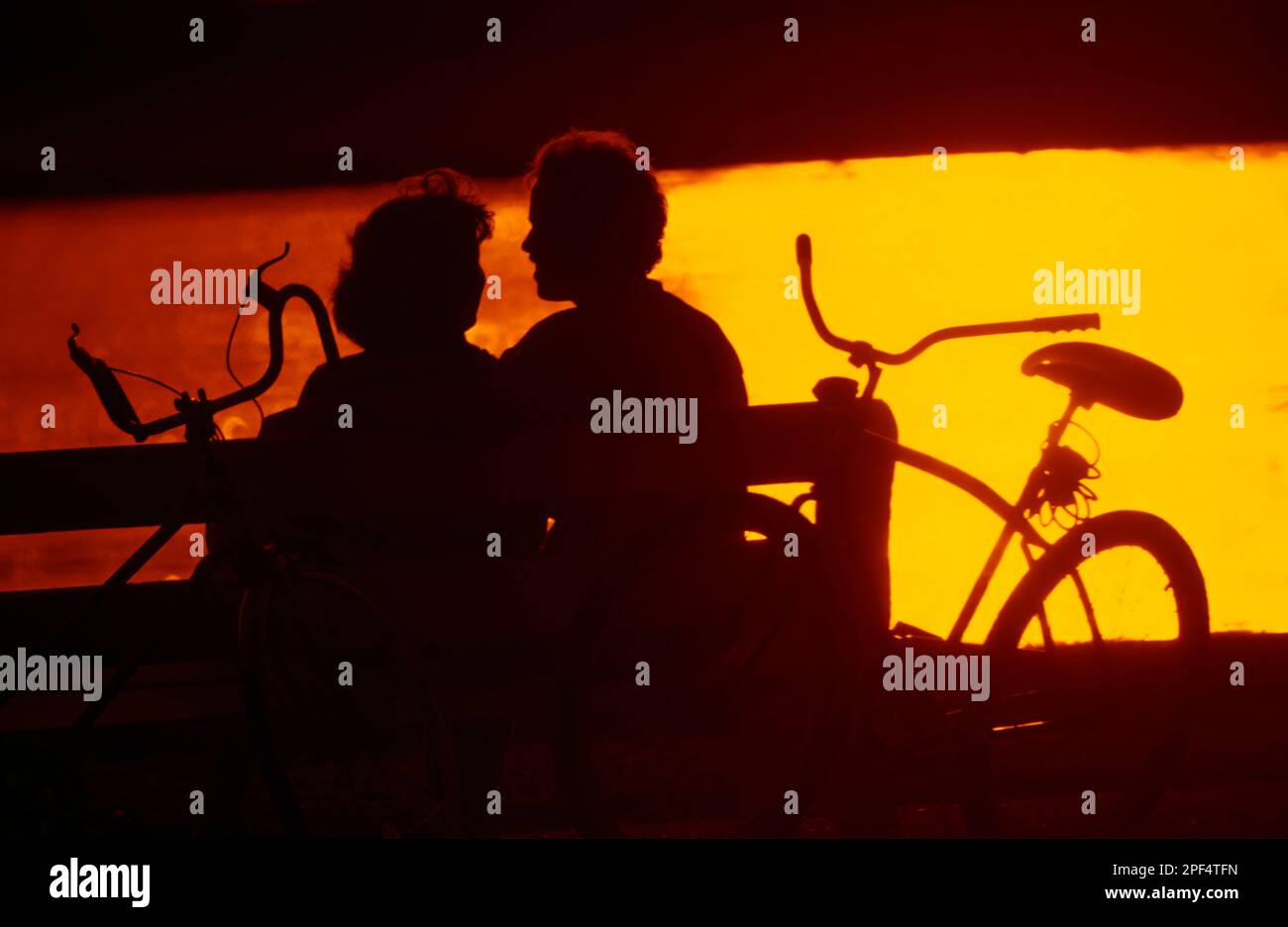 Silhouette of young couple relaxing on a park bench after riding their ...