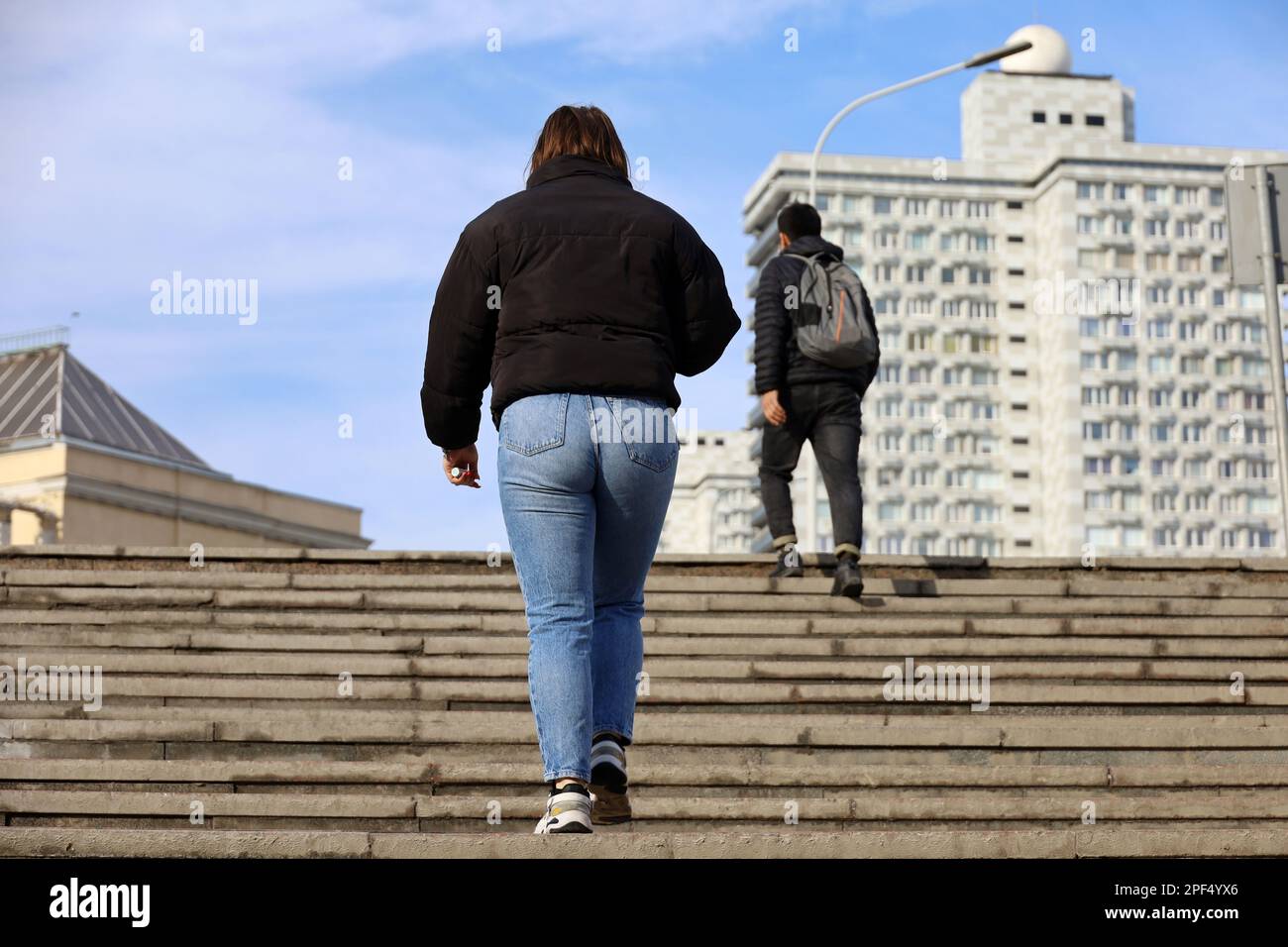 Girl wearing jeans and jacket going up the stone stair, rear view. Female fashion and footwear in spring city Stock Photo