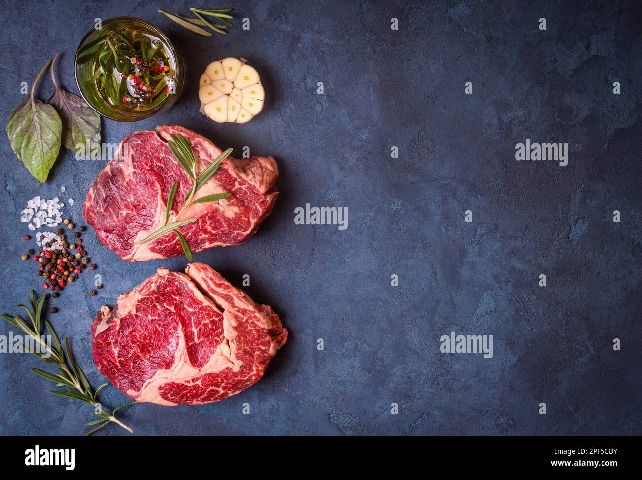 Raw juicy ribeye steaks with seasonings ready for roasting on rustic