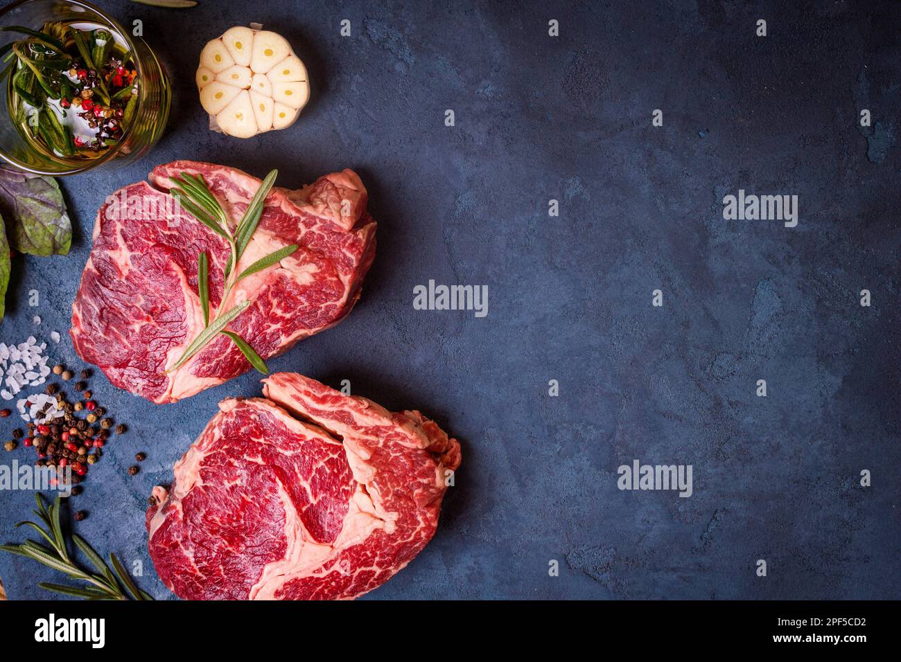 Raw juicy ribeye steaks with seasonings ready for roasting on rustic ...