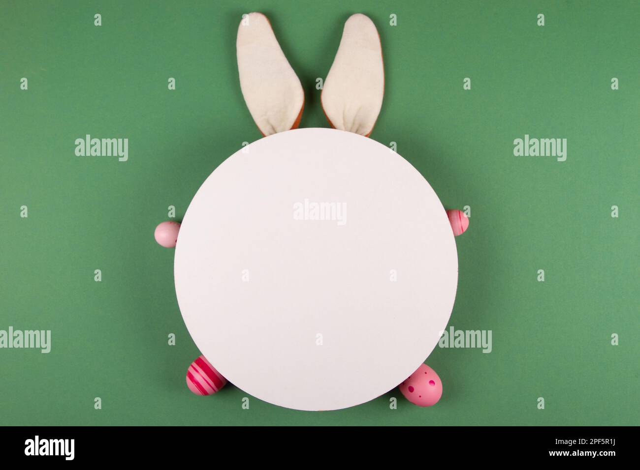 Easter eggs, white circles, and bunny ears decorate a green background Stock Photo