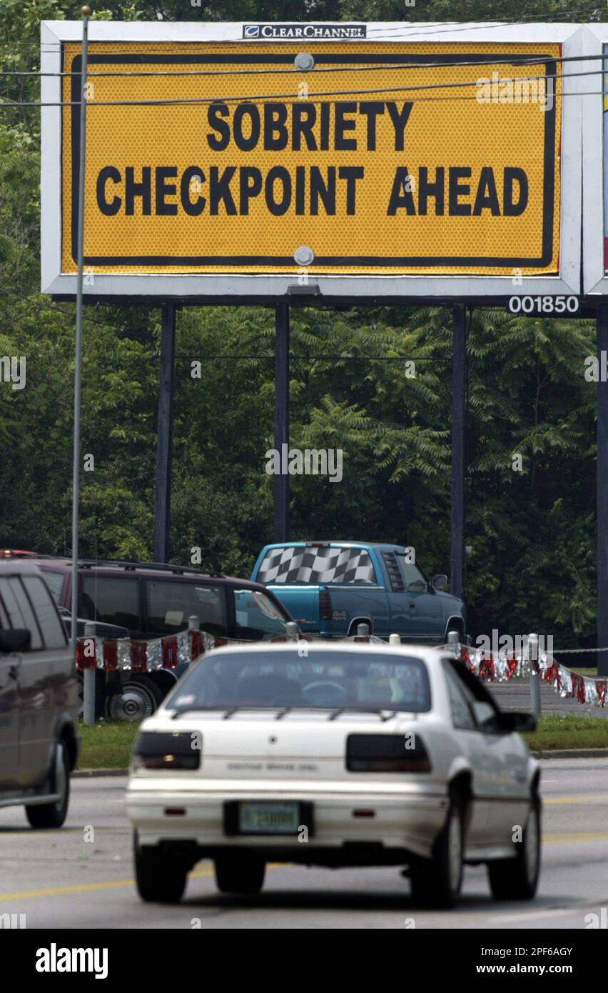 A motorist approaches a billboard "Sobriety Checkpoint Ahead" on the near west side of