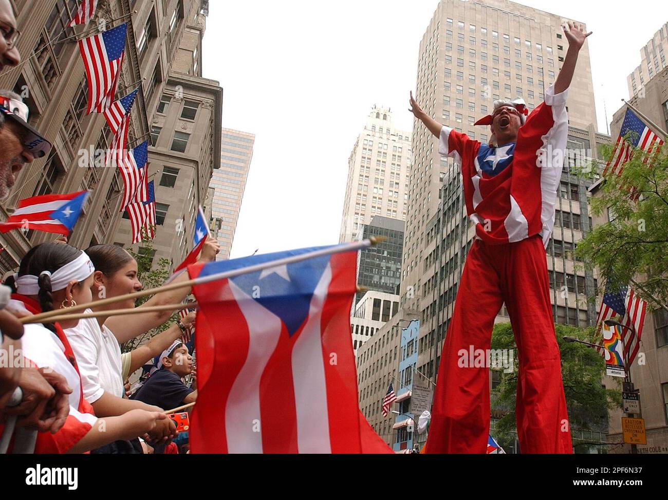 A man on stilts wearing the colors of Puerto Rico walks along Fifth