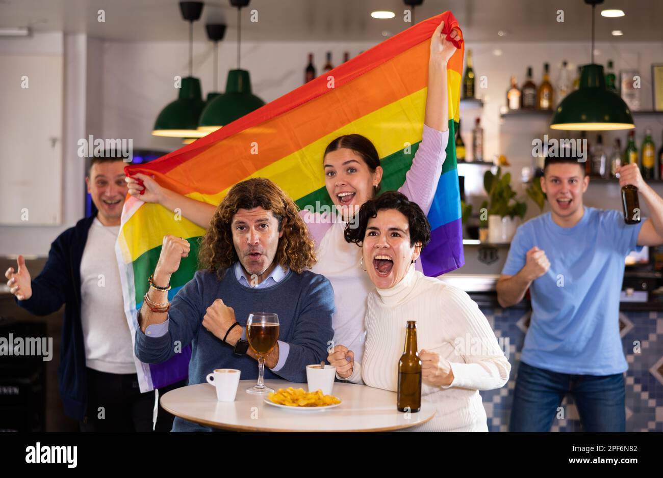 Happy friends of different ages with LGBT flag drinking beer and celebrate victory of your