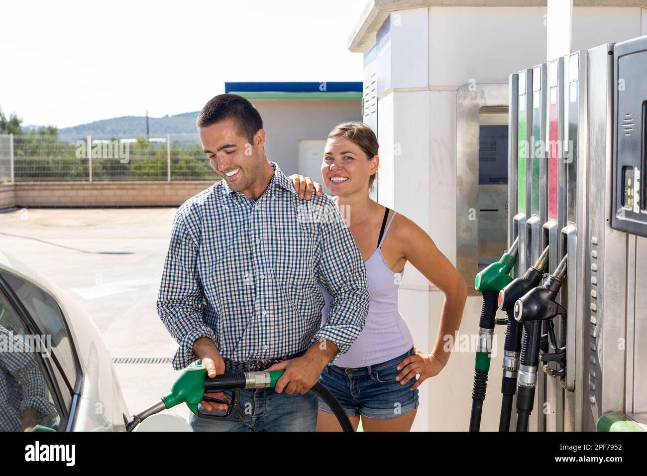 Positive couple filling up tank of their car with gasoline in gas