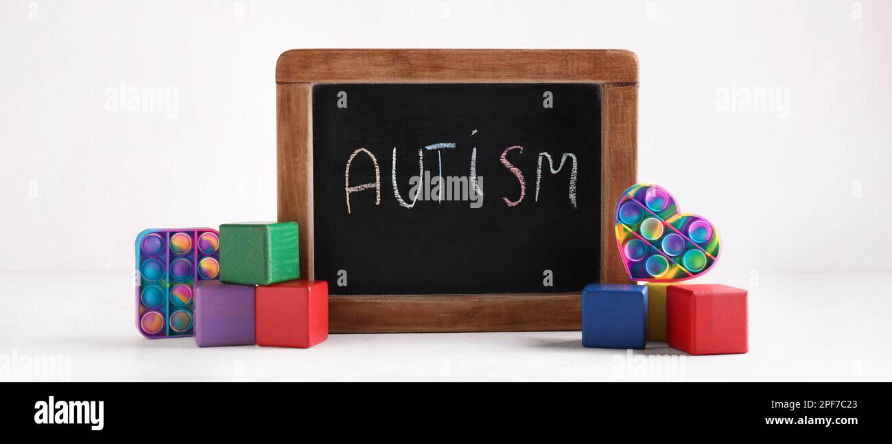 Chalkboard with word AUTISM, cubes and pop it fidget toys on white background Stock Photo