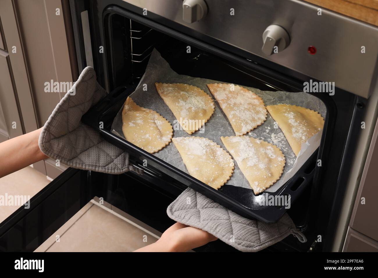 Woman putting baking sheet with meat empanadas into oven, closeup Stock Photo