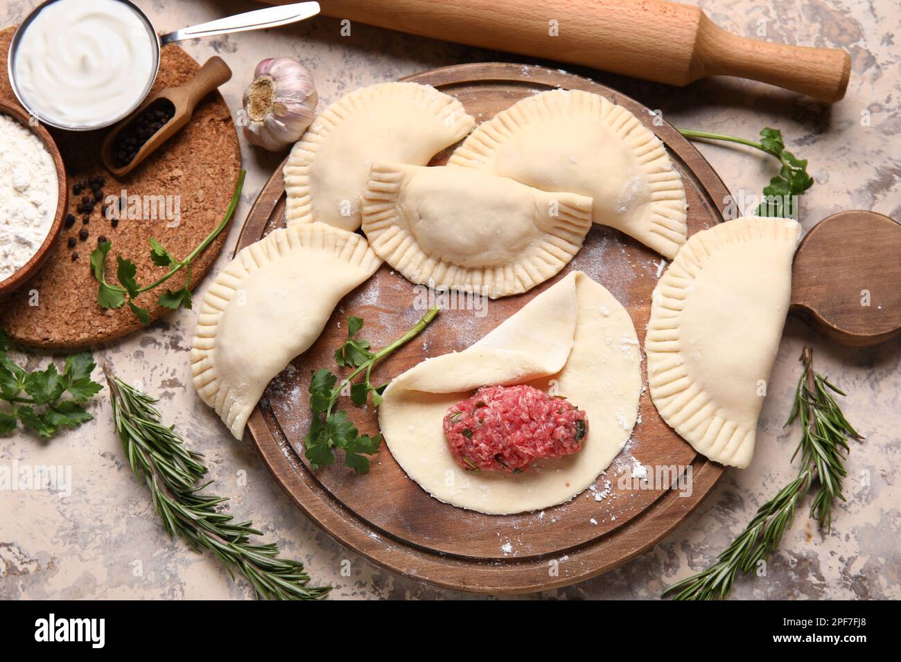 Wooden board with raw meat empanadas and ingredients on light