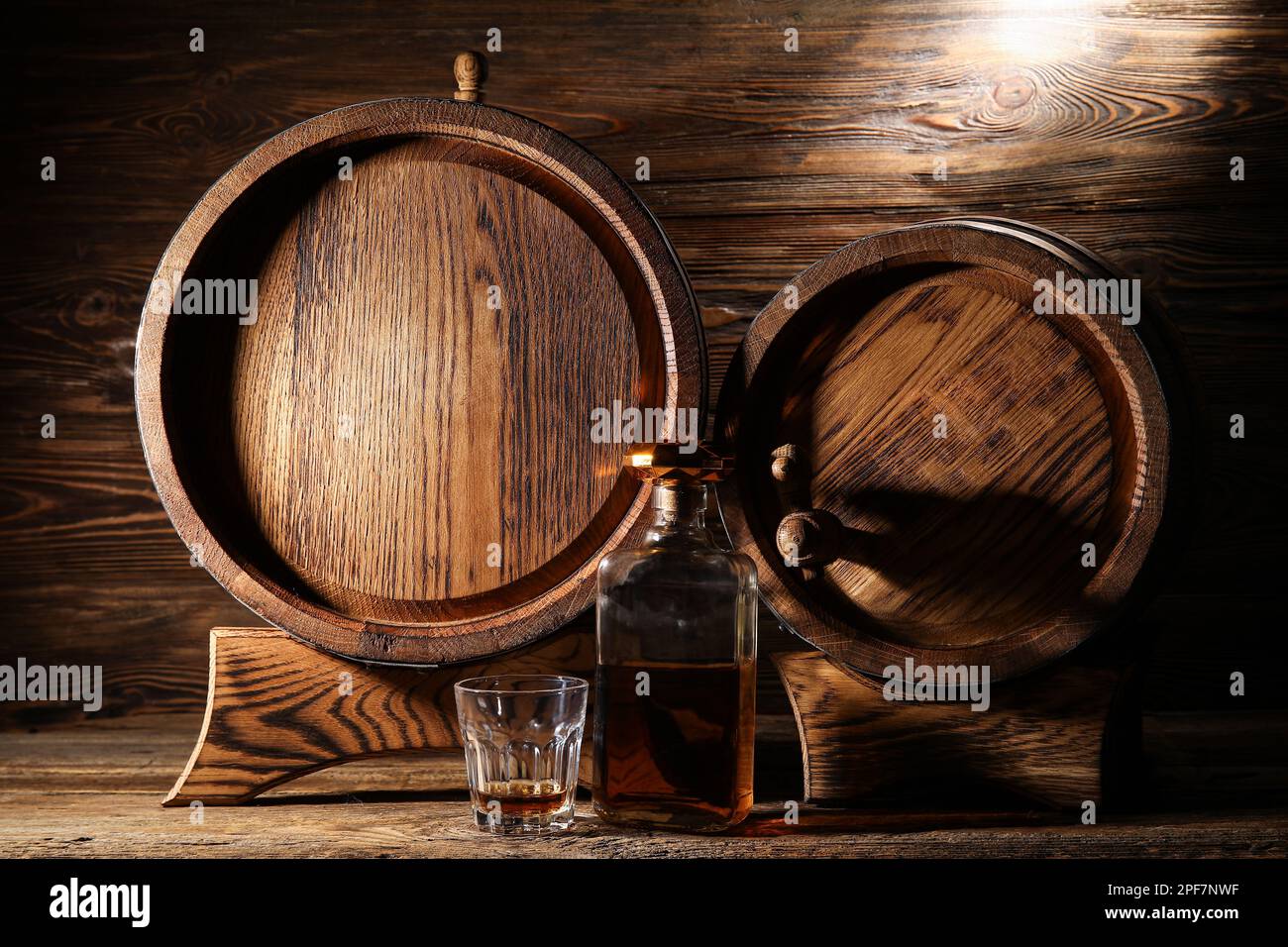 Bottle and glass of tasty whiskey with oak barrels on wooden background Stock Photo
