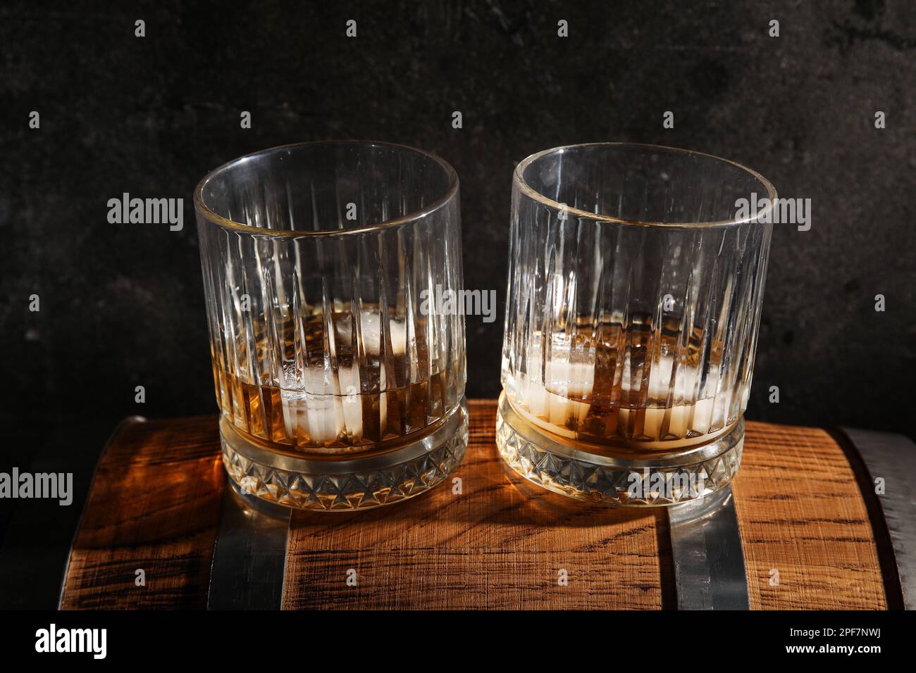Glasses of cold whiskey on wooden barrel against dark background Stock Photo