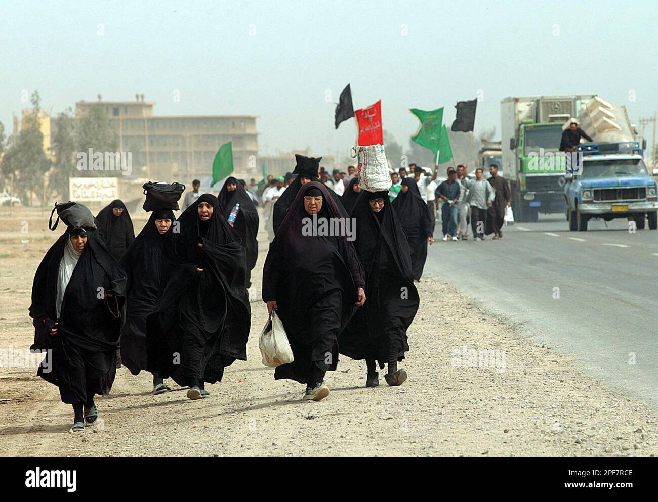 Iraqi Shiite Muslim women walk in front of men carrying flags with  religious slogans, on the highway linking Baghdad with the southern city of  Karbala on Saturday, April 19, 2003. For the