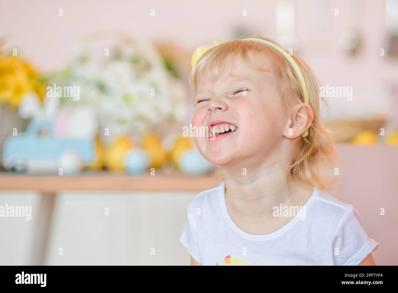 Adorable happy little blonde girl with short hair in white dress with in kitchen on Easter day Stock Photo