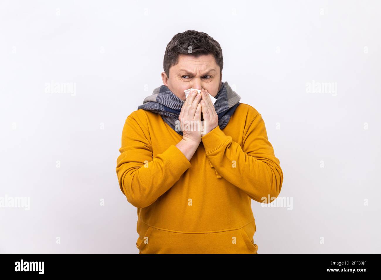 Man in warm scarf coughing sneezing hard in napkin, feeling unwell with runny nose, severe