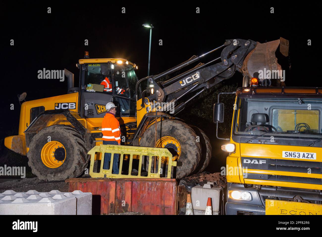 A DAF gritter truck being loaded by a JCB digger at night in Denby Dale, West Yorkshire Stock Photo