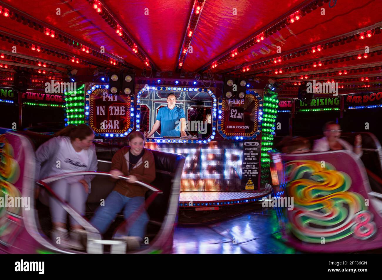 Teenage girls on a fairground waltzer ride with the operator in the booth behind Stock Photo