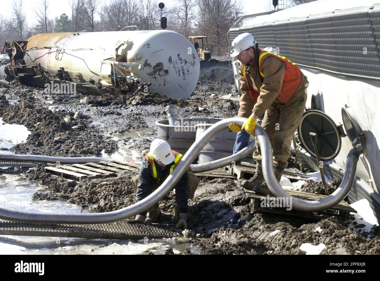 Recovery workers position suction hoses to empty a rail car of plastic