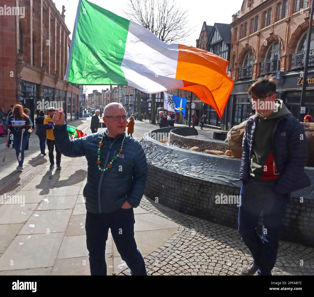 Man waves Irish flag - St Patricks Day 2023 Irish Community parade Orford Ln Warrington to Bridge Street IRA bombing memorial, Cheshire, UK Stock Photo