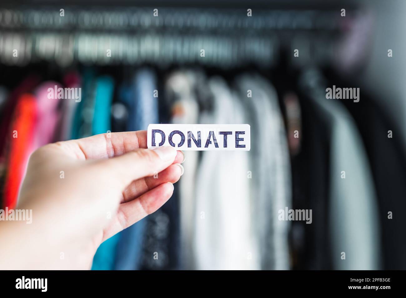 Donate sign held in front of wardrobe full of clothes, concept of excessive shopping and consumerism Stock Photo