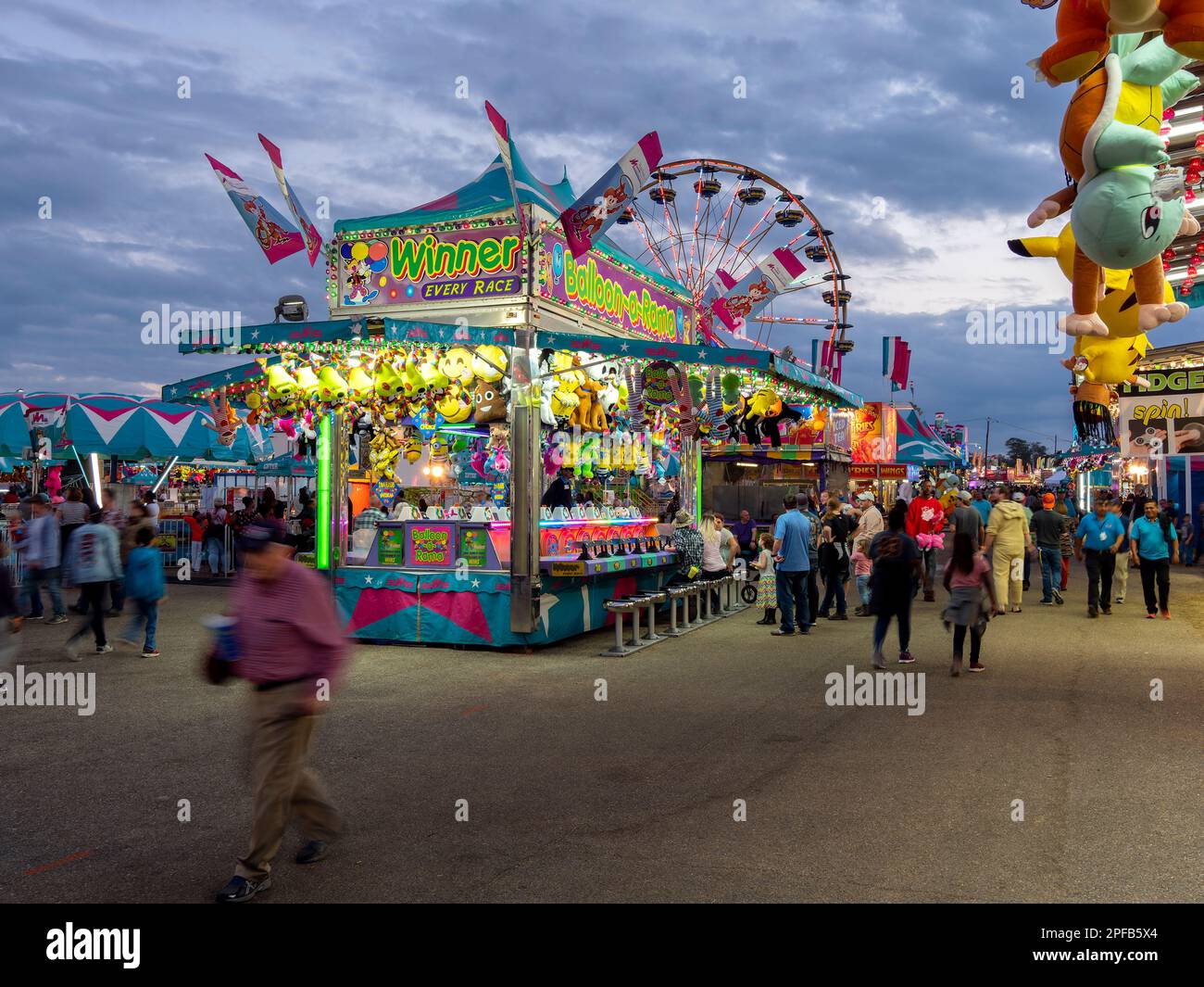 Carnival midway with people and families walking past and playing games at booths with colorful prizes at the National Fair in Montgomery Alabama, USA. Stock Photo