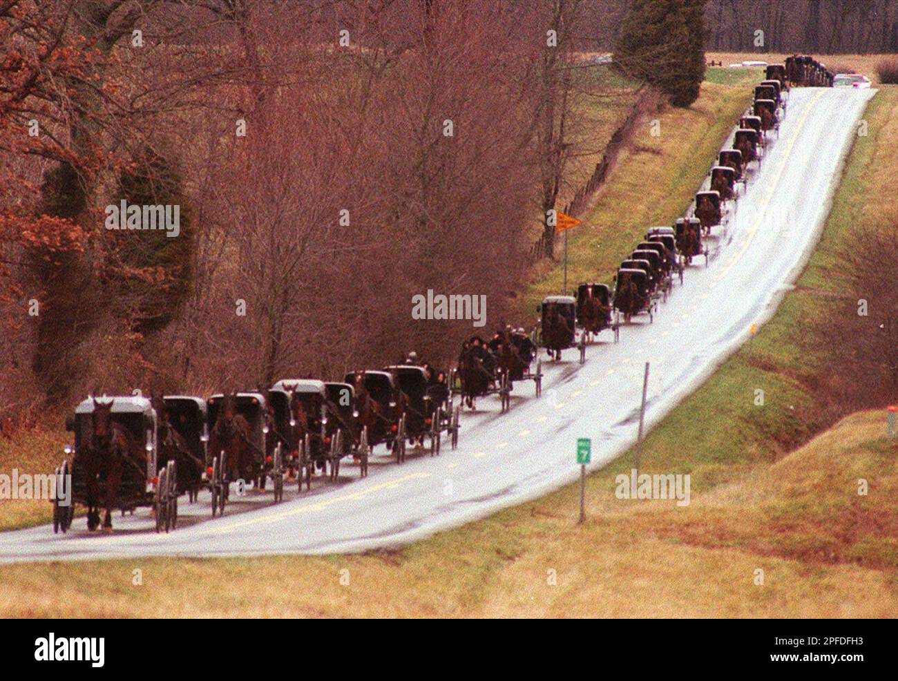 An Amish funeral procession of horse drawn buggies moves along Kentucky