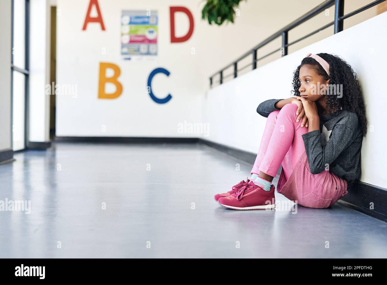 Where are my parents. Full length shot of a young girl sitting alone in the hallway at school and feeling depressed. Stock Photo