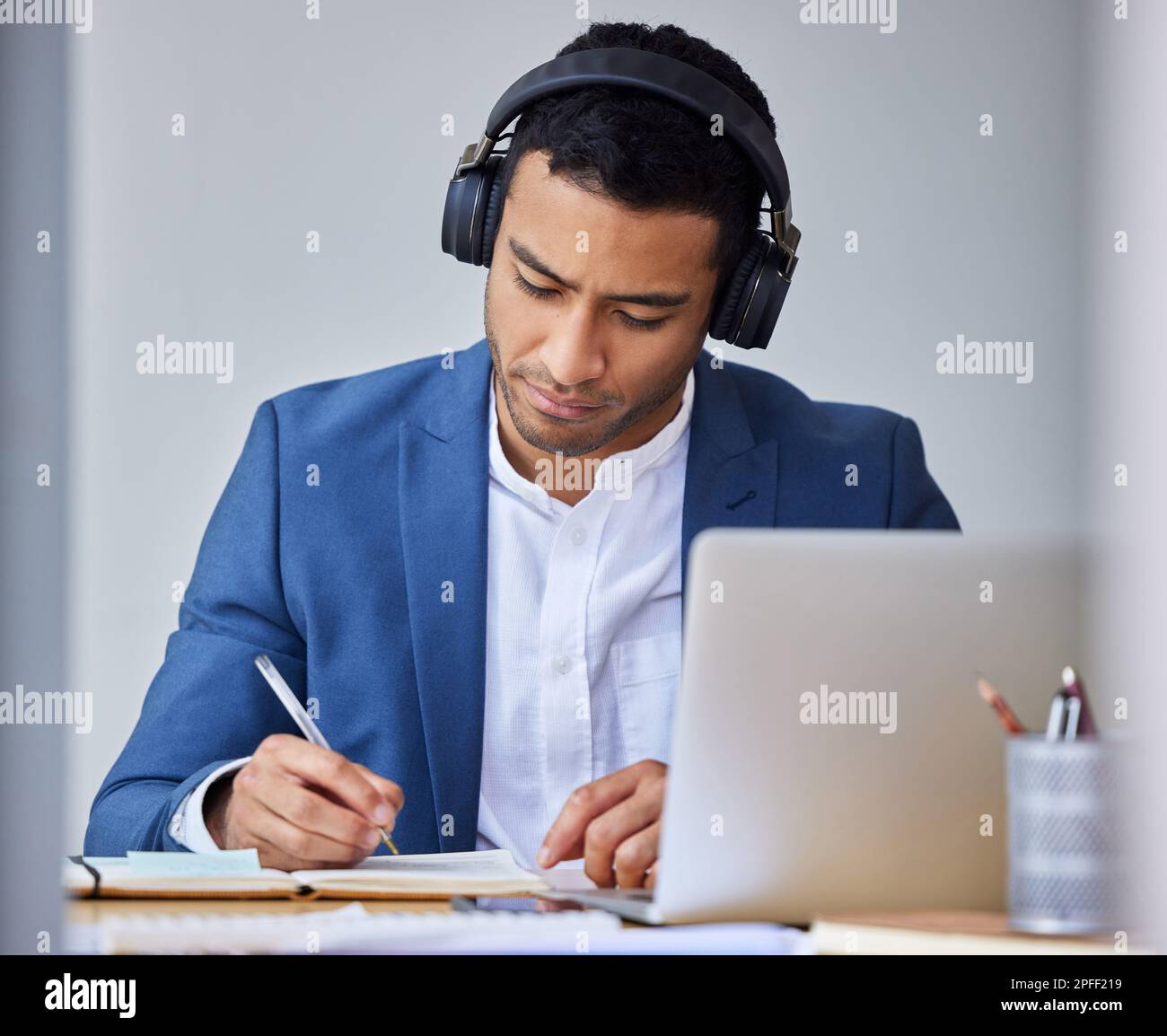 Taking important notes. a young businessman taking notes while using his laptop. Stock Photo