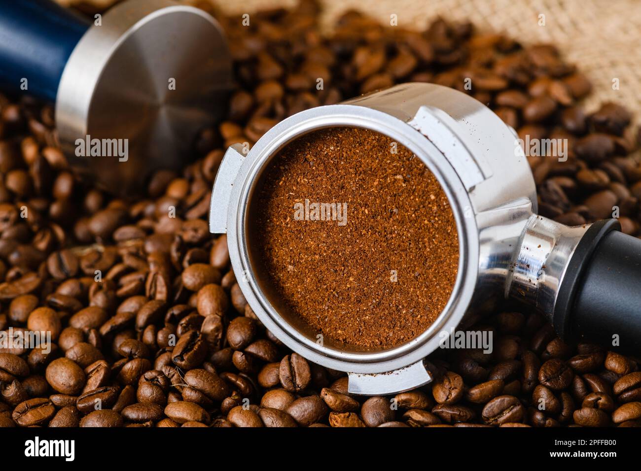 Amped puck of coffee grounds within a basket of portafilter and coffee beans spilled on the