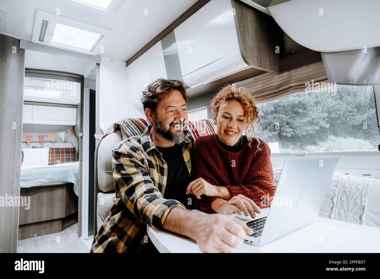 Happy travel couple lifestyle smile and use laptop together inside a modern camper van in vanlife offgrid alternative office workplace. Adventure life Stock Photo