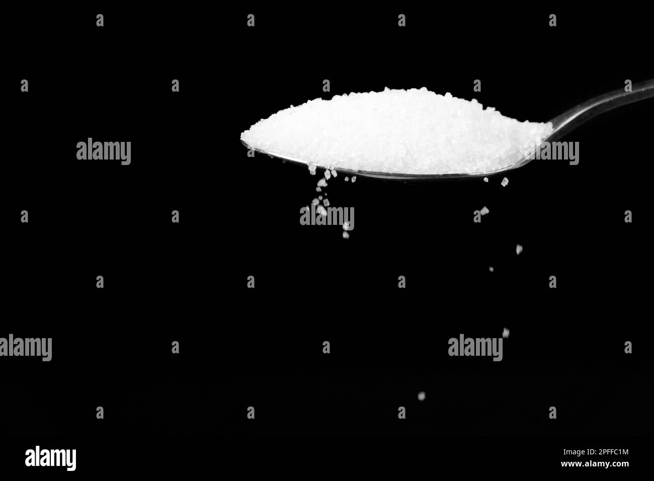 Macro photography of a teaspoon with crumbling white sugar on a black background, copy space. Stock Photo