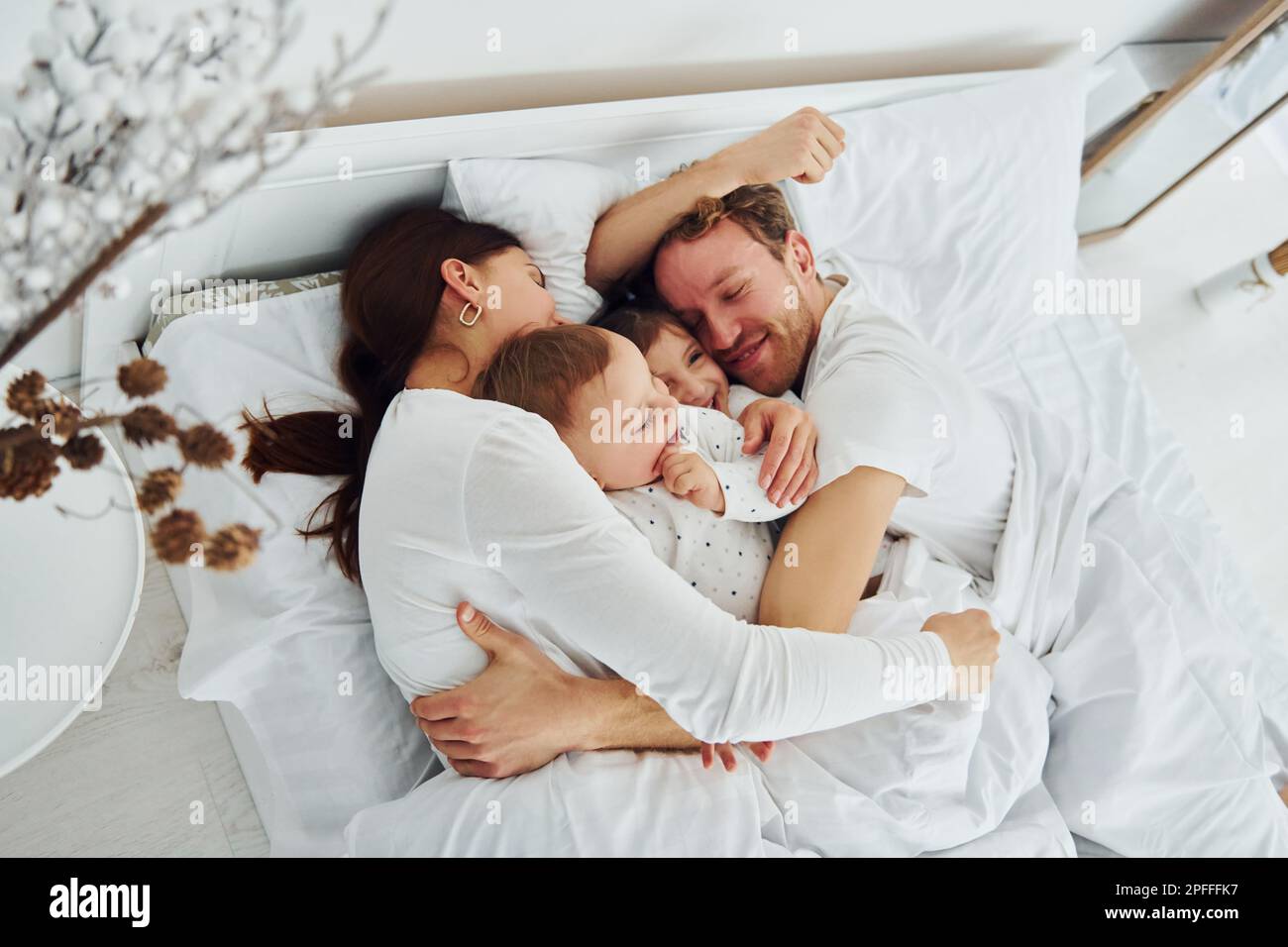 Woman and man lying down on bed with their children. Interior and ...