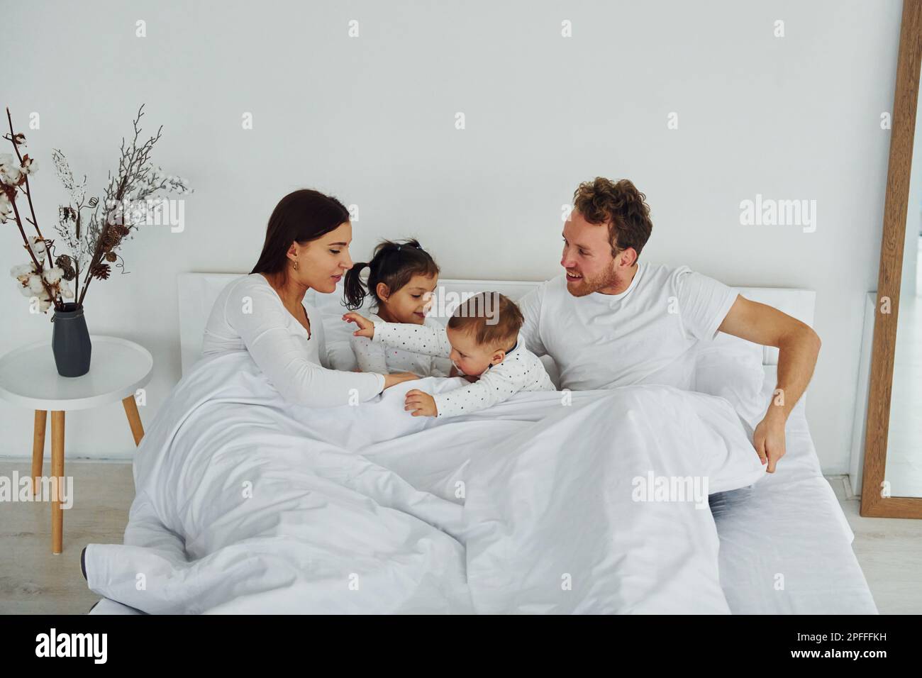 Woman and man lying down on bed with their children. Interior and ...
