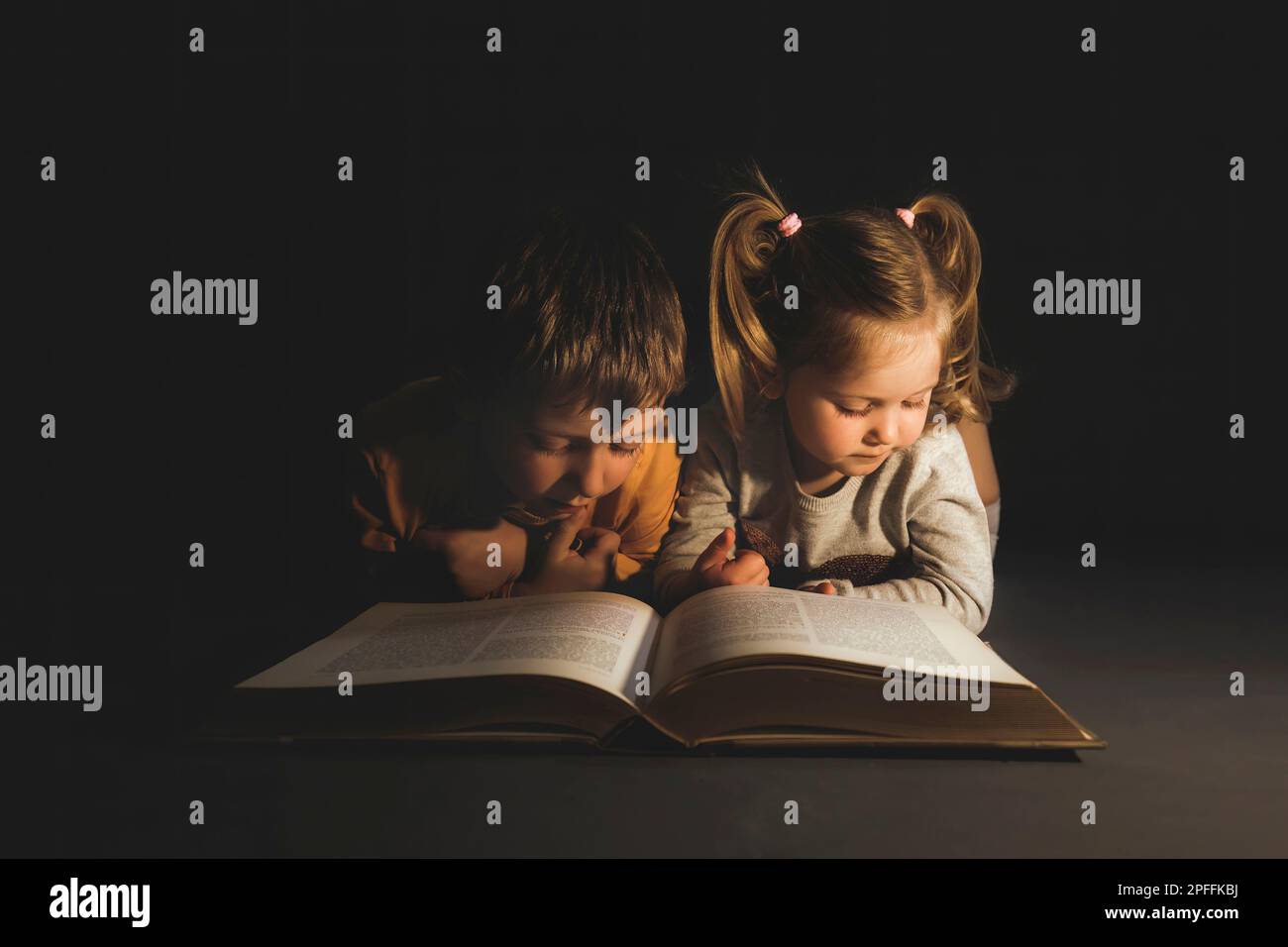 children lying in the dark reading a book Stock Photo
