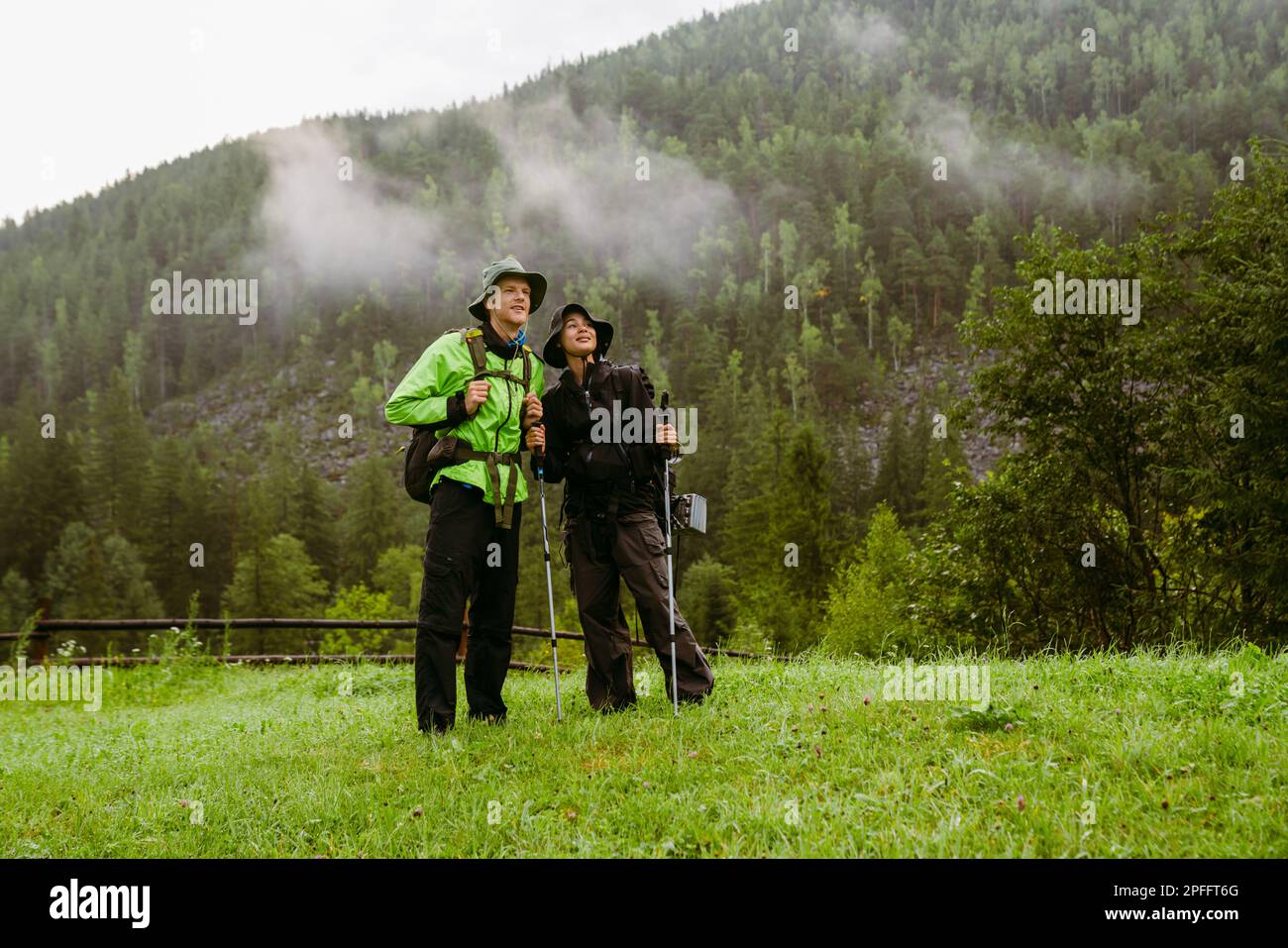 Young smiling multiethnic tourist couple with backpacks hiking in mountains Stock Photo
