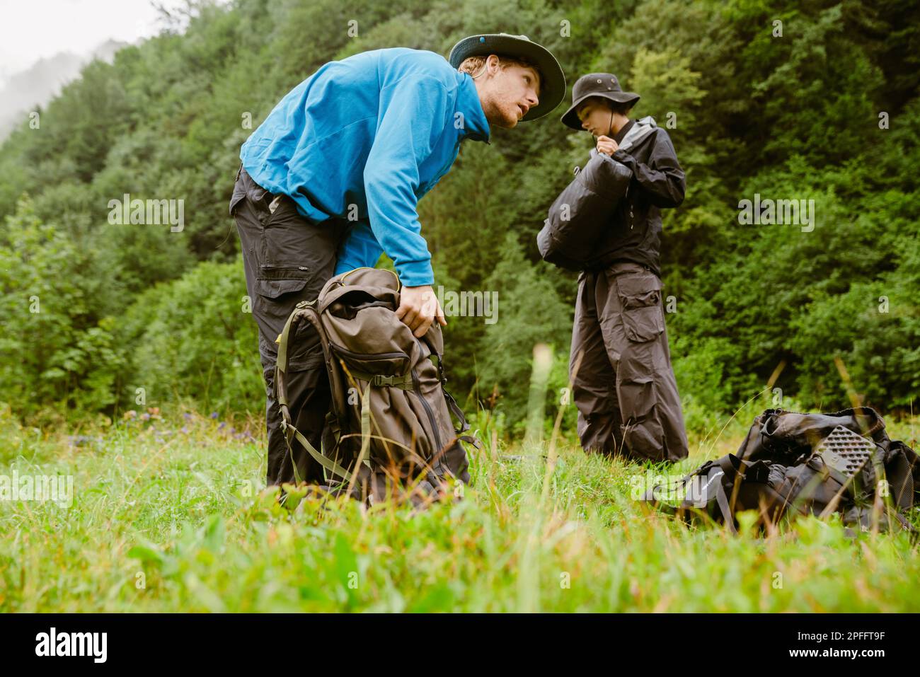 Young white people wearing trekking equipment using backpacks while hiking in mountain forest Stock Photo