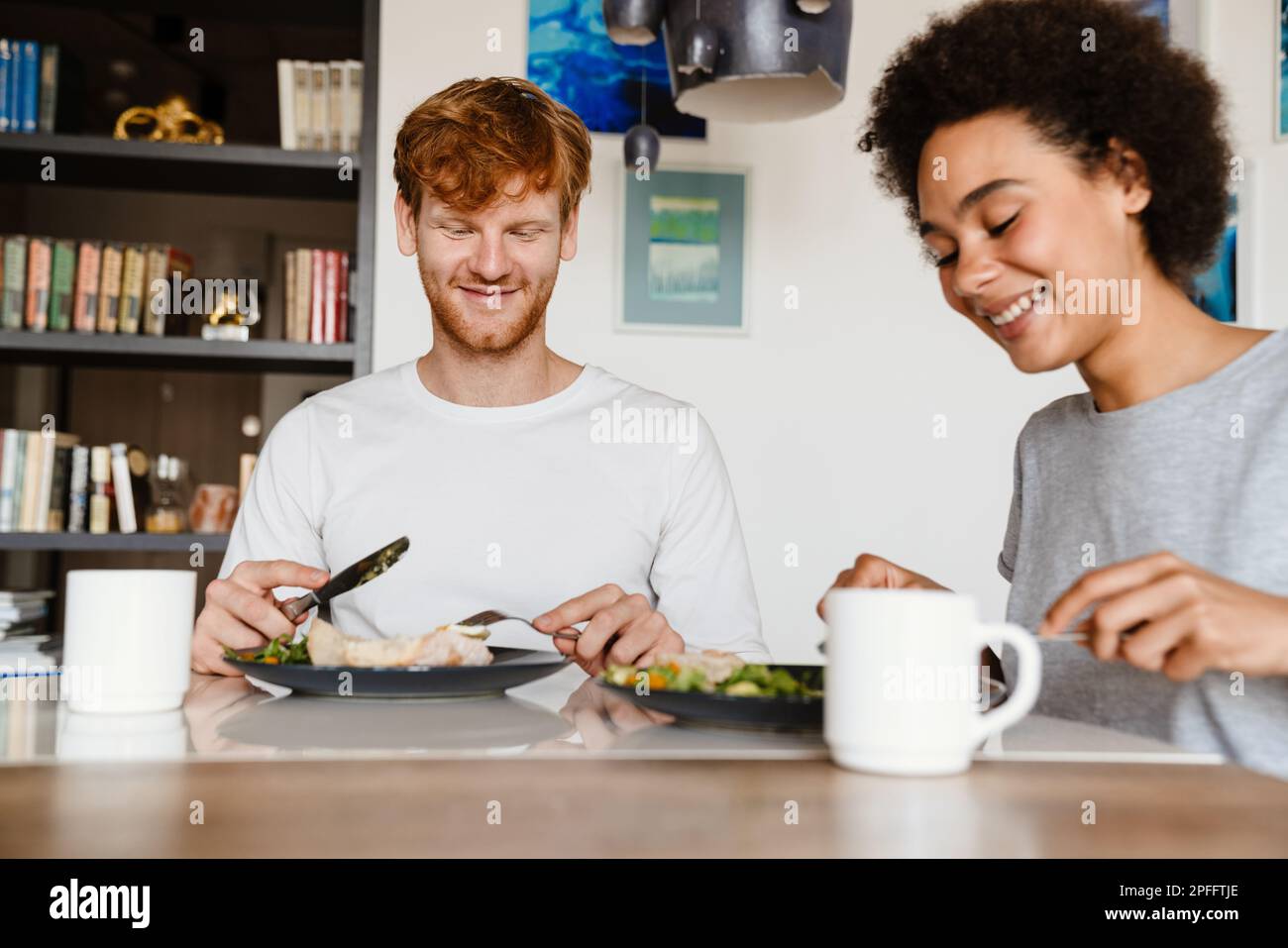 Young beautiful smiling happy interracial couple eating breakfast together sitting at home Stock Photo
