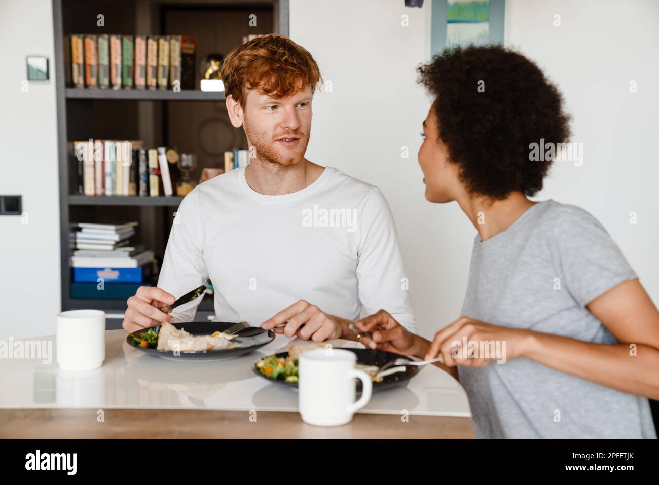 Young beautiful interracial couple looking at each other and eating breakfast together at home Stock Photo