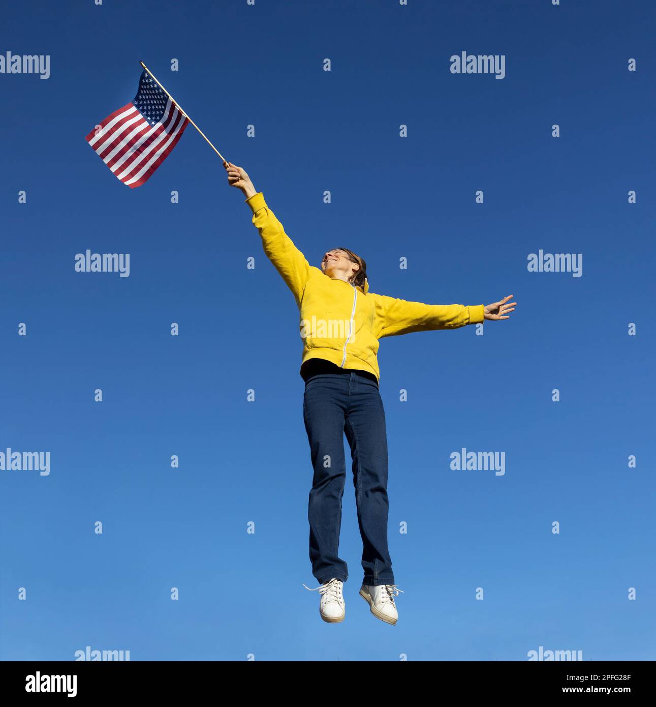 happy active woman jumping joyfully against cloudless blue sky. Raise the American flag in hand. United States Independence Day celebration. take off Stock Photo