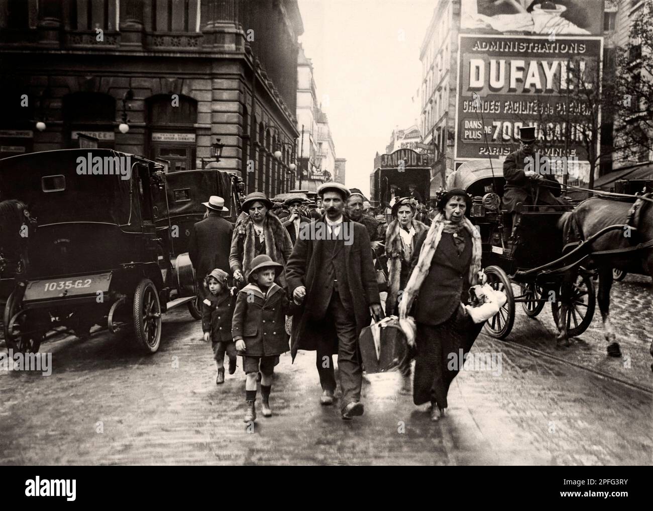 French Immigration - 'Here is a train coming from the north, we see several families who, terrified by the raid of the Germans, come to ask for hospitality'. Family with luggage (men, women and children) walking up a street with their luggage in the middle of road traffic. Horse-drawn carriages, coachman. Immigration. First World War. Paris. Great War. War of 14-18. North Station? Stock Photo