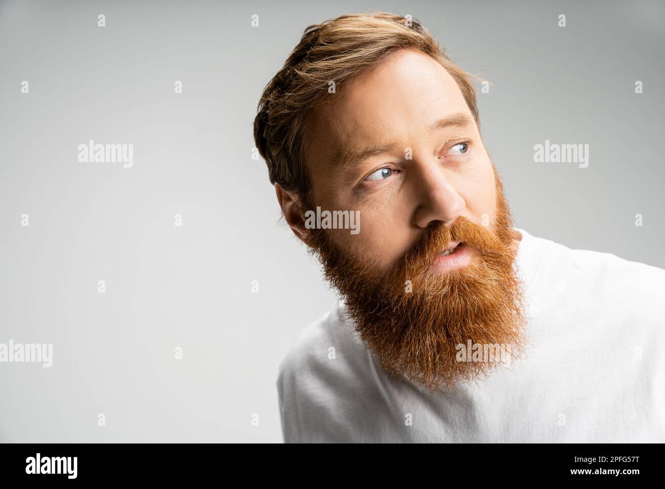 curious man with beard wearing white t-shirt looking away isolated on grey,stock image Stock Photo